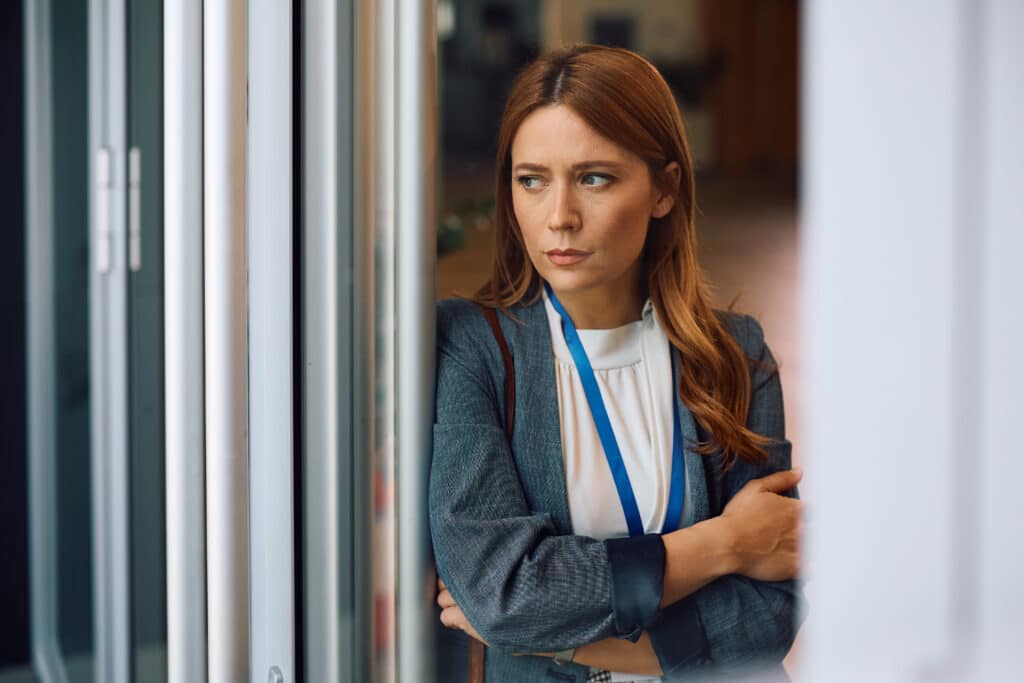 Worried businesswoman standing by the window in the office and looking through it. Uncertainty at work.